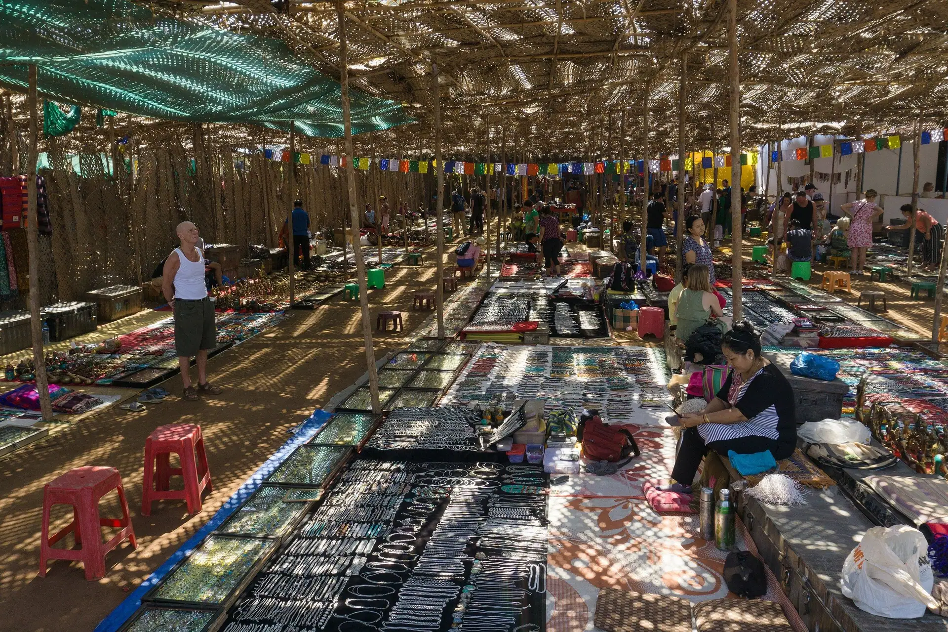 Rows of jewellery and craft stalls under a woven shade canopy at the Anjuna flea market, North Goa