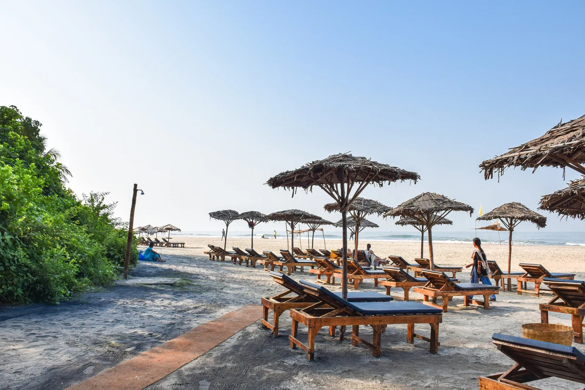 Wooden sun loungers under thatched umbrellas lining the sand at Ashwem Beach, North Goa