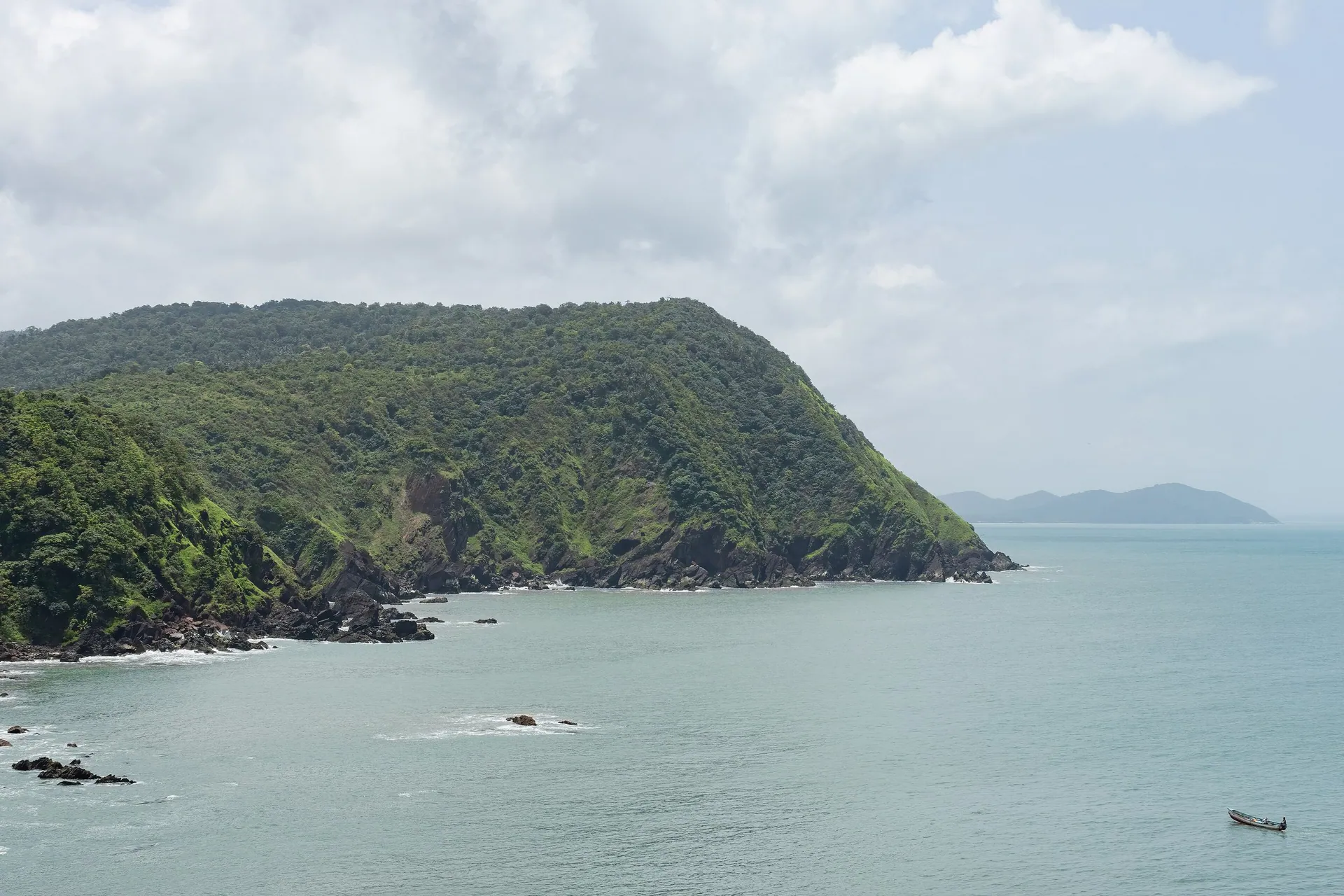 A boat on the Arabian Sea below a green headland, seen from Cabo de Rama fort