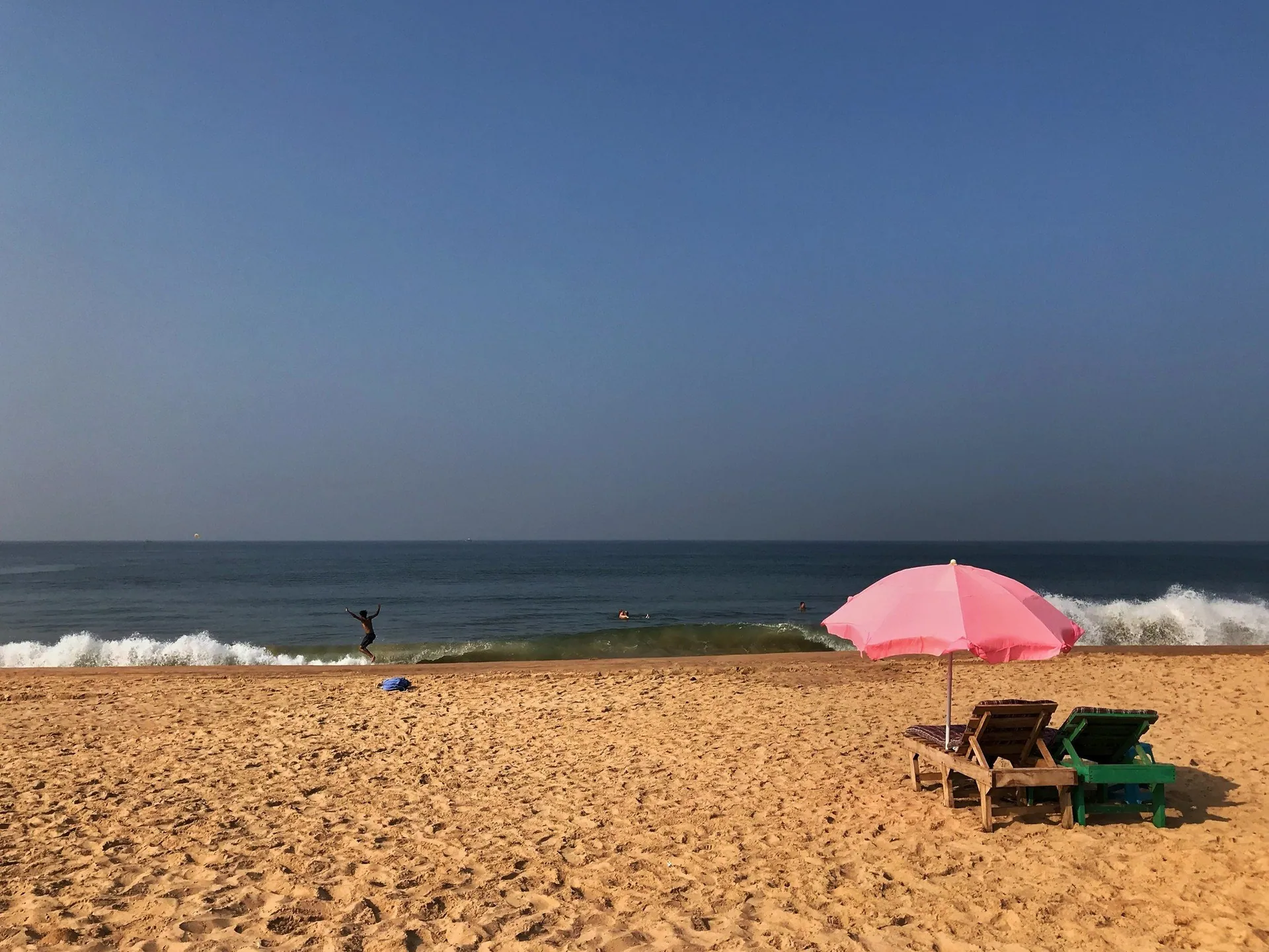 A pink beach umbrella and two loungers on golden sand at Calangute Beach, with surf breaking beyond