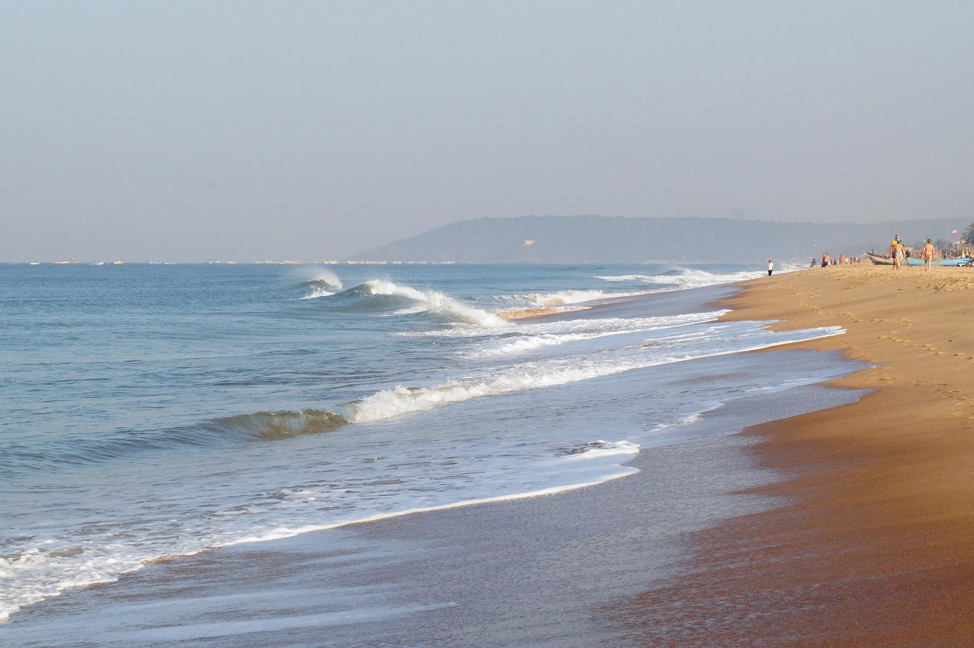 Waves running up the golden sand of Candolim Beach, with a distant headland in the haze, North Goa