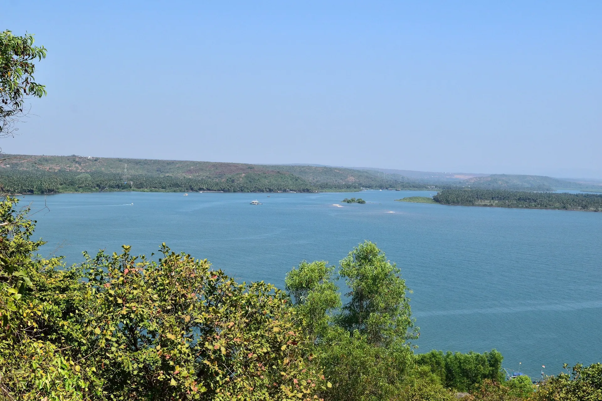 The broad Chapora river seen from a wooded hillside, with low green hills on the far bank, North Goa