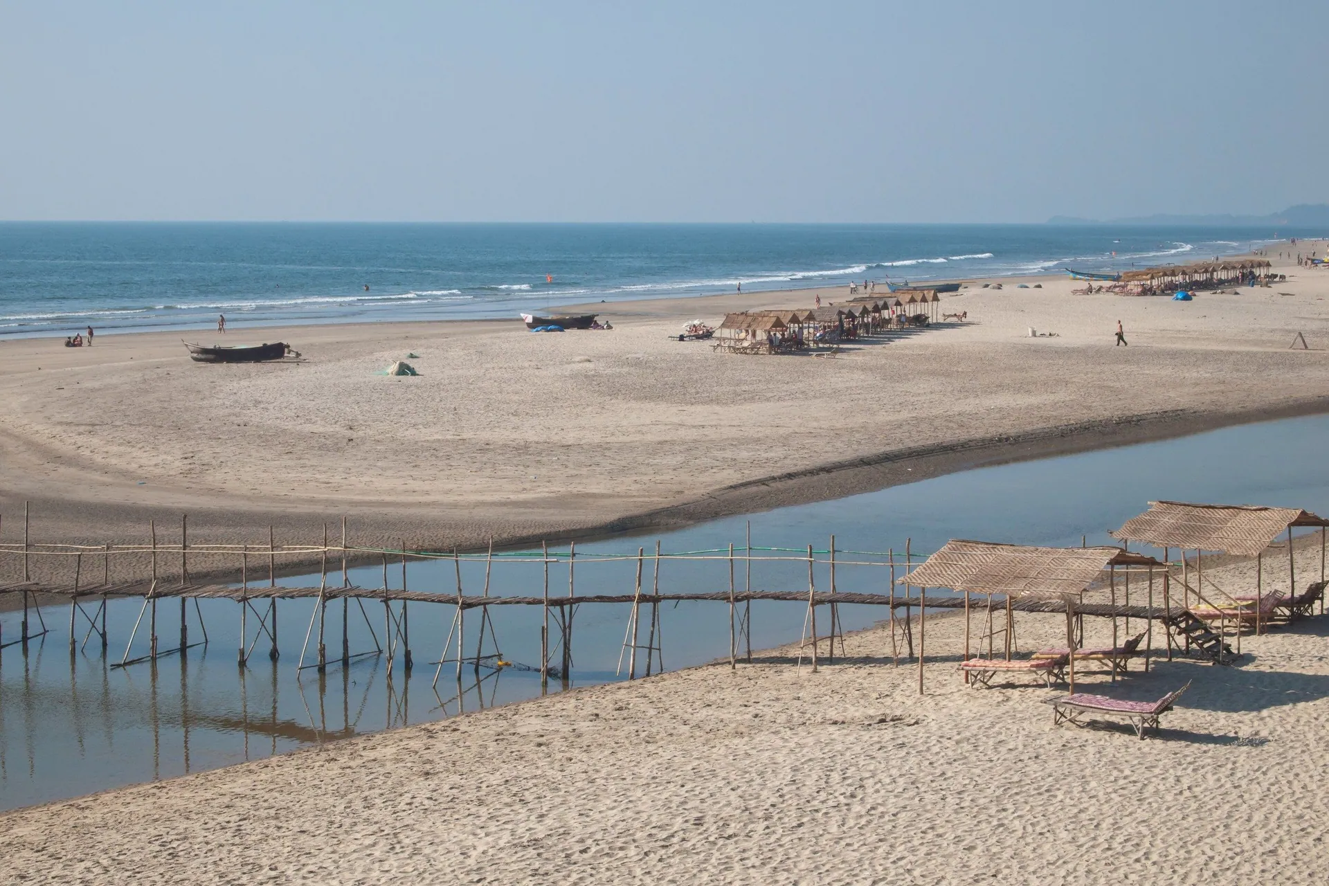 A bamboo footbridge over the Mandrem river to the wide sands and thatched shelters of Mandrem Beach