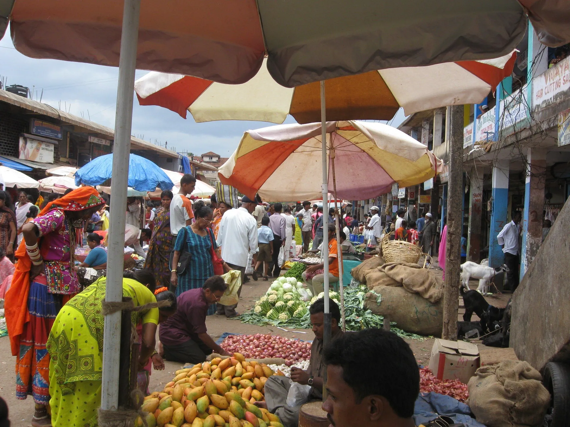 Fruit and vegetable vendors under faded striped umbrellas at the busy Mapusa market, North Goa