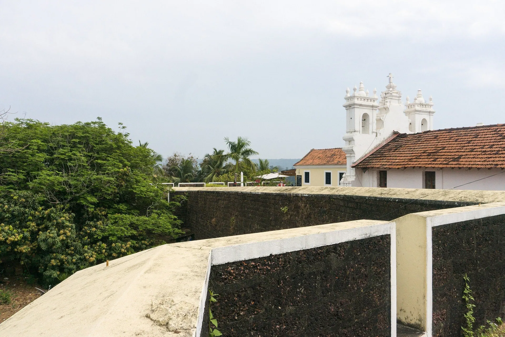 Laterite ramparts of Fort Tiracol with the white towers of its church rising behind, northern tip of Goa